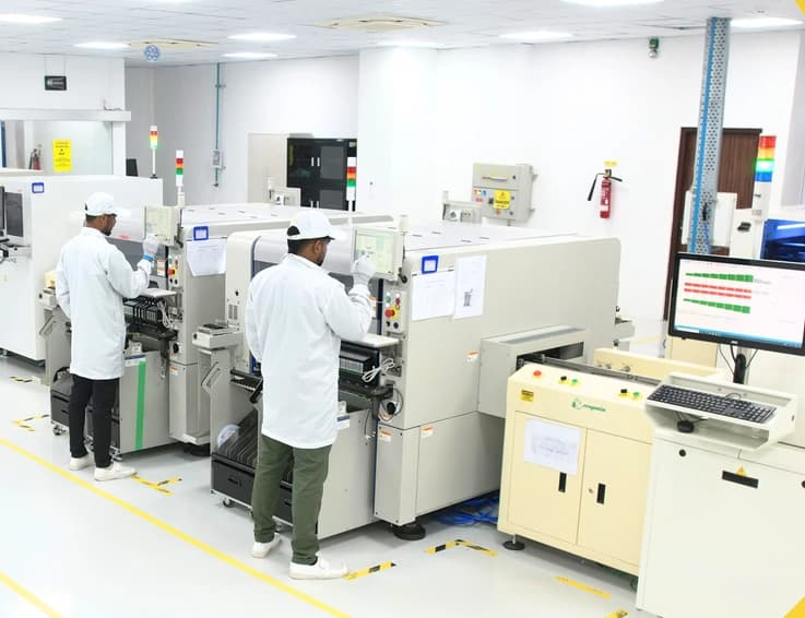 Technicians operating automated production machines in a cleanroom hardware manufacturing facility.