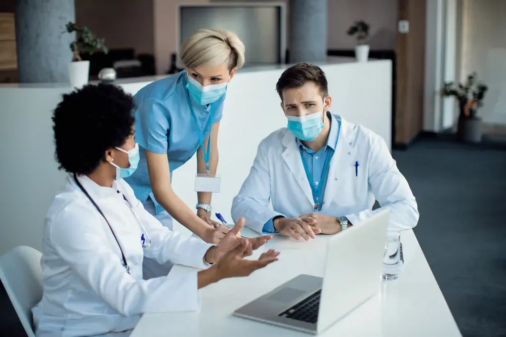 Medical team collaborating around laptop in hospital, showcasing healthcare innovation powered by ai services.